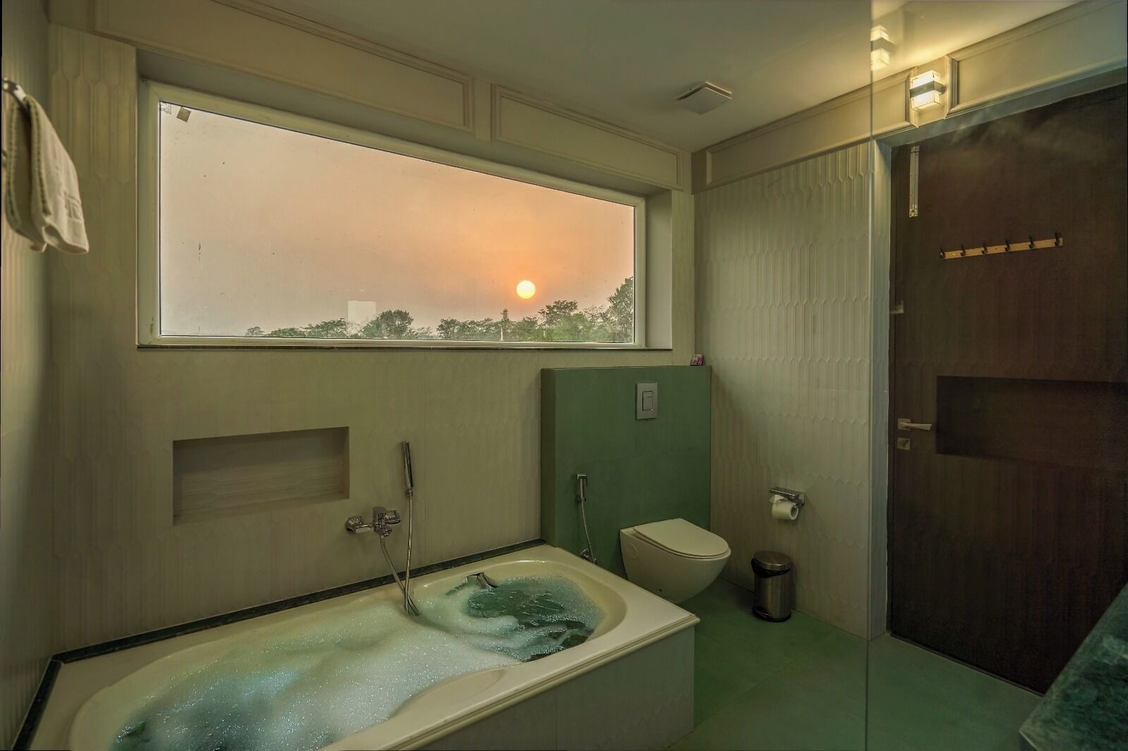 A bathroom with a bathtub, toilet, and a window overlooking a cityscape.
