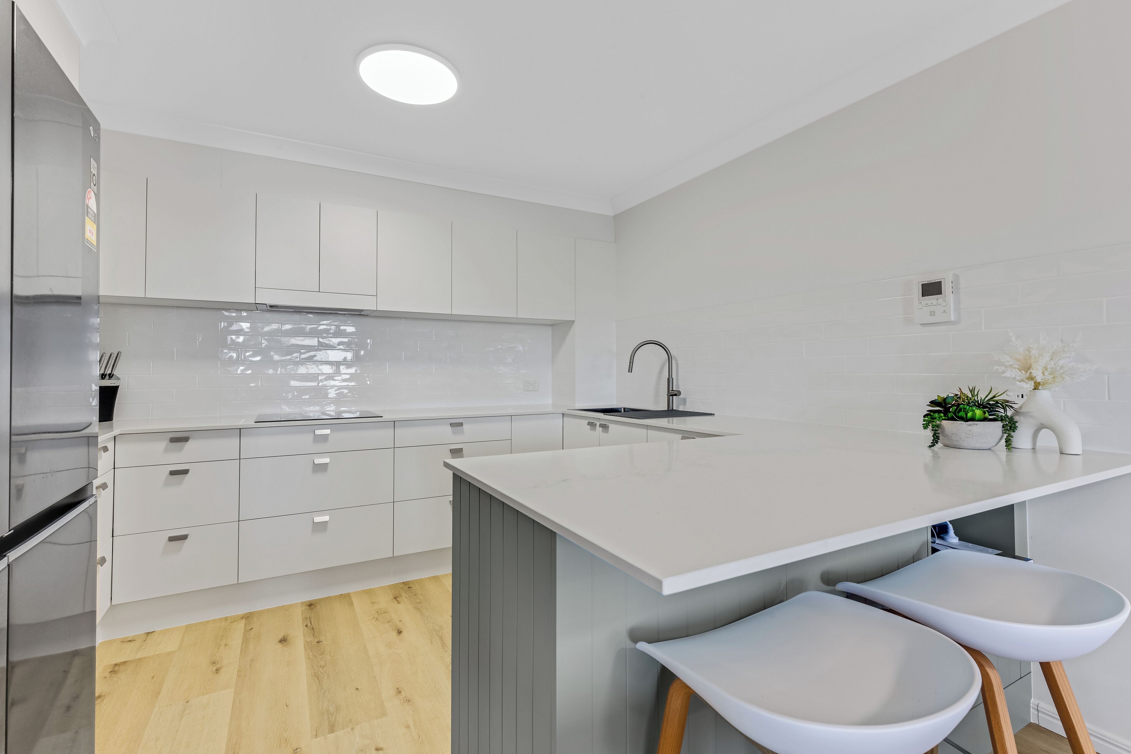 A modern kitchen with white cabinetry, a central island with stools, and a built-in oven.