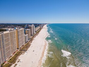 A coastal hotel with multiple high-rise buildings, a sandy beach, and a clear blue sea.