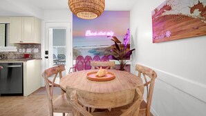 Una cucina con mobili bianchi, un tavolo da pranzo in legno con quattro sedie, un lampadario in vimini e decorazioni a tema spiaggia.