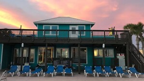 Un edificio fronte spiaggia con un balcone, sedie blu e un cartello.