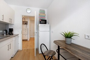 A compact kitchen with white cabinets, a microwave, a coffee maker, and a dining area with a bench and potted plant. - Südstrand Magic near the South Beach with Balcony and Wi-Fi (Wilhelmshaven)