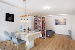 A dining area with a table set for two, a bookshelf, and a bed in the background. - Südstrand Magic near the South Beach with Balcony and Wi-Fi (Wilhelmshaven)