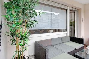 A balcony with a wicker sofa, a glass table, and a bamboo plant. - Südstrand Magic near the South Beach with Balcony and Wi-Fi (Wilhelmshaven)