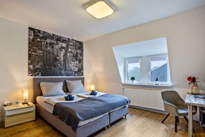 Un dormitorio con cama, mesitas de noche, ventana, una silla y una obra de arte con vista urbana.