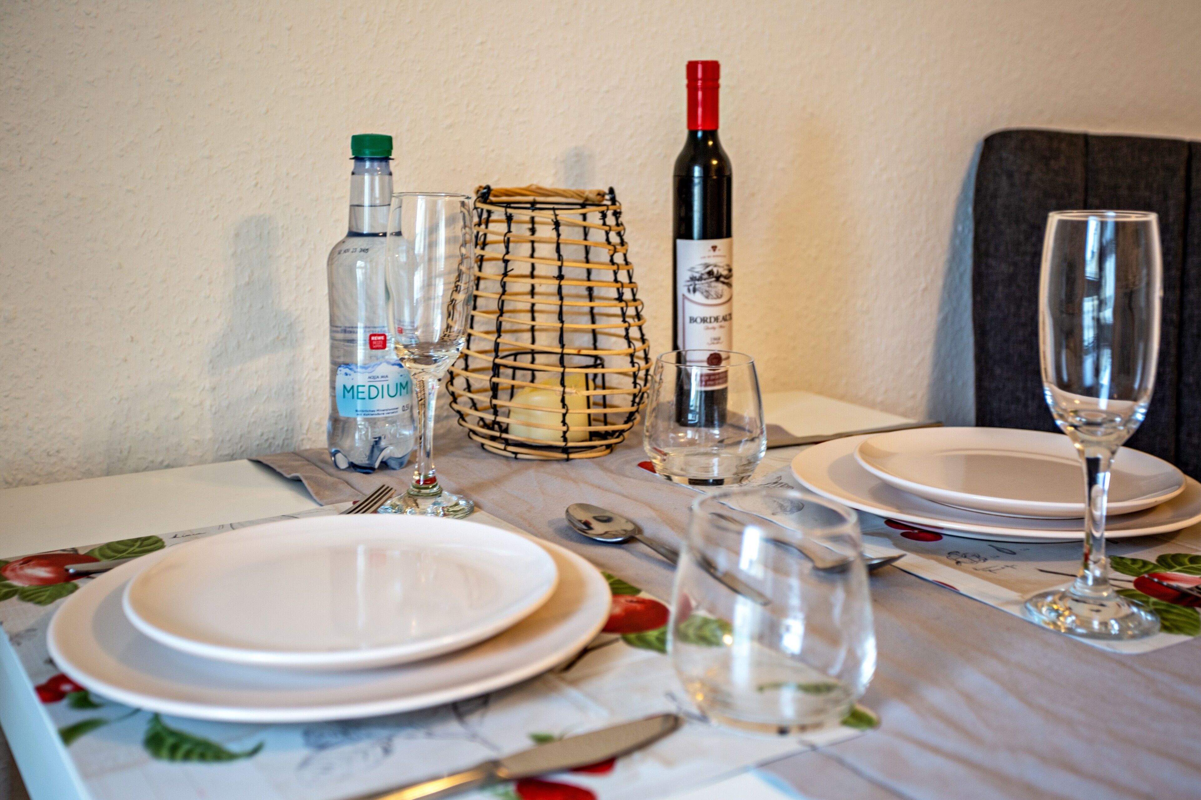 Ett bord dukat med tallrikar, bestick, en vinflaska, glas och en vattenflaska.