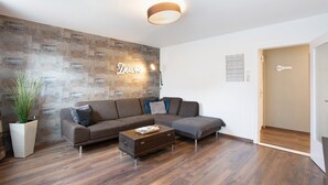 A modern living room with a sectional sofa, a small coffee table, a potted plant, and a wall with a 'Dream' sign. - Coastal Love Apartment – Close to Park & City (Wilhelmshaven)