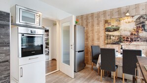 A compact kitchen with a microwave, oven, and refrigerator, a dining area with a table and chairs, and a wall with a coffee-themed mural. - Coastal Love Apartment – Close to Park & City (Wilhelmshaven)