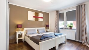 A bedroom with a bed, bedside tables, a lamp, a window with curtains, and a radiator. - Coastal Love Apartment – Close to Park & City (Wilhelmshaven)