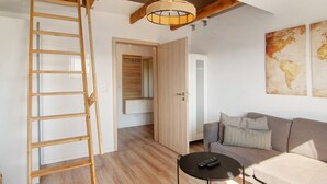 A room with a wooden ladder, a sofa, a small round table, and a hanging light fixture.