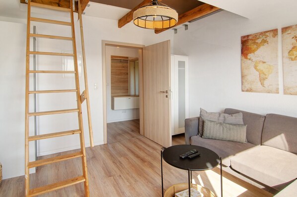 A room with a wooden ladder, a sofa, a small round table, and a hanging light fixture.