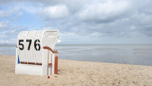A beach chair labeled '576' on a sandy beach with a cloudy sky.