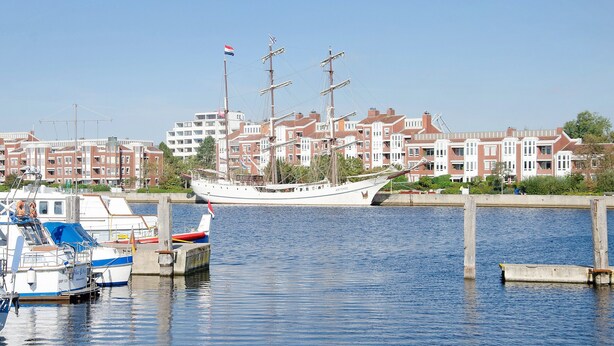 A marina with a large sailing ship docked, surrounded by residential buildings.