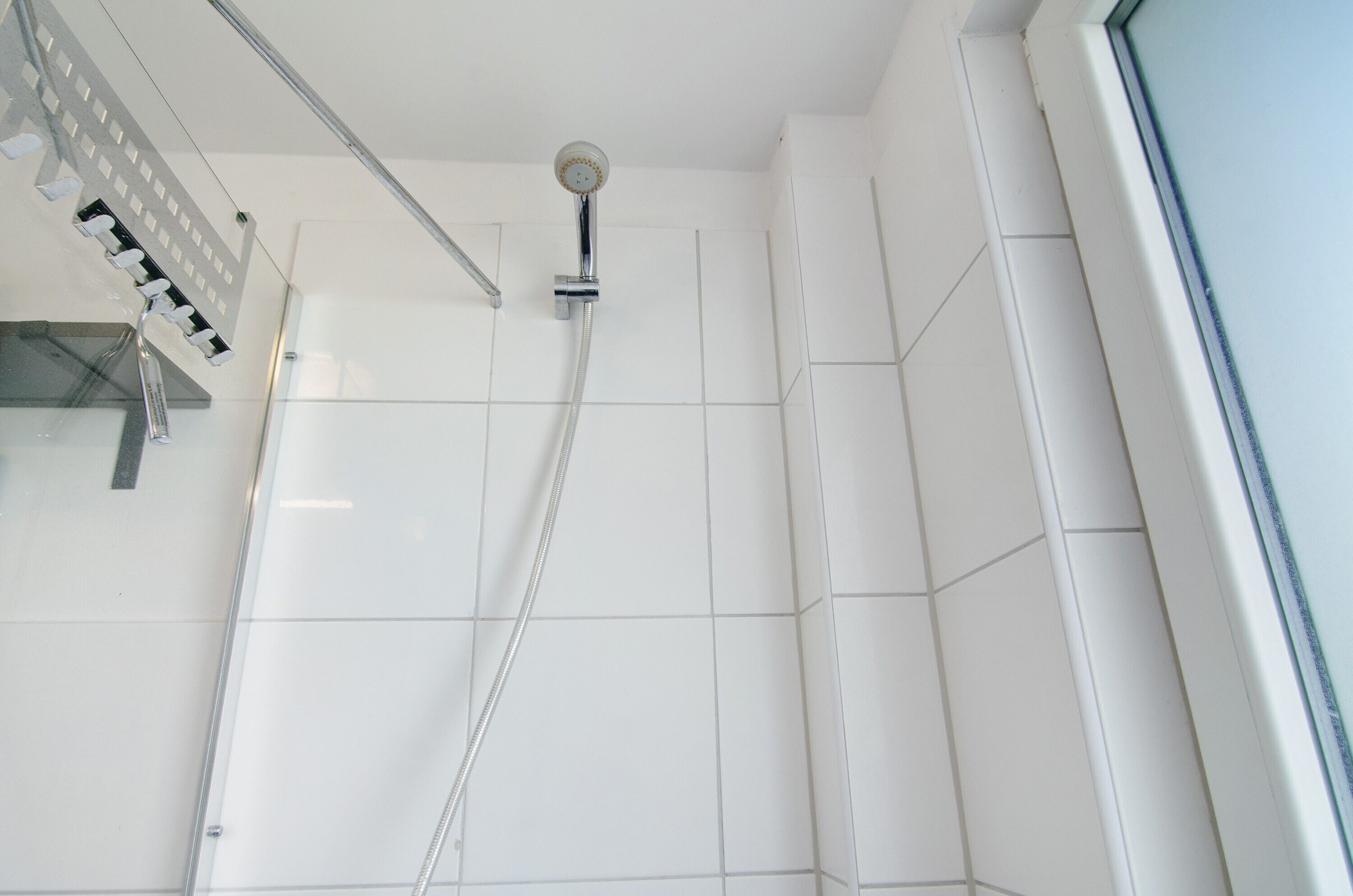 Eine moderne Dusche mit Handbrause, Glasabtrennung und weißen Fliesen.