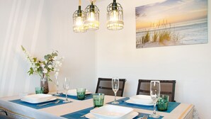 A dining table set with plates, glasses, and cutlery, with a vase of flowers and a painting of a beach scene on the wall.