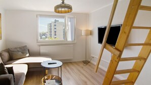 A living room with a sofa, a small round table, a wicker basket, a wooden ladder, a floor lamp, and a TV mounted on the wall.
