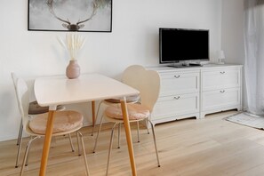 Une chambre moderne avec une table blanche, deux chaises, un téléviseur et un meuble.