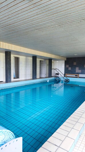 A swimming pool with tiled walls and a wooden ceiling, a bench, and a staircase leading to an upper level.