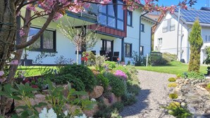 A residential area with a house featuring a modern design, a gravel driveway, and a variety of flowering plants.