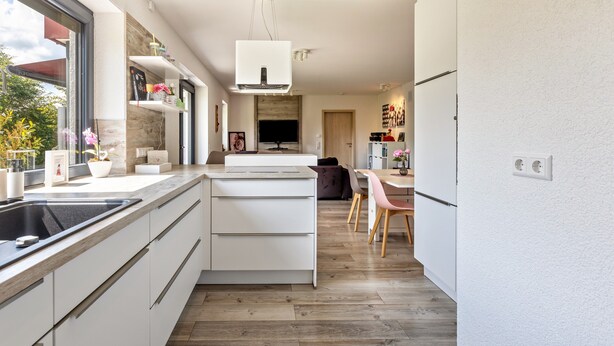 A modern kitchen with white cabinetry, a built-in oven, and a large window.