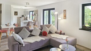 A modern living room with a sectional sofa, a round coffee table, and a dining area with a white table and chairs.