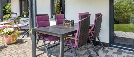 A patio with a table and chairs, a potted plant, and a view of the garden.