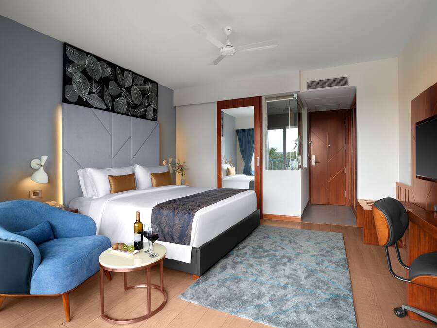Habitación de hotel moderna con una cama grande, un escritorio, una silla, un televisor y un ventilador de techo.