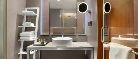 A modern bathroom with a white sink, mirror, and shelves with towels.