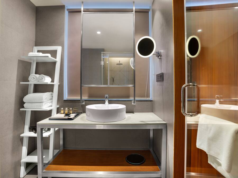 Un baño moderno con lavamanos, espejo y estantes con toallas.