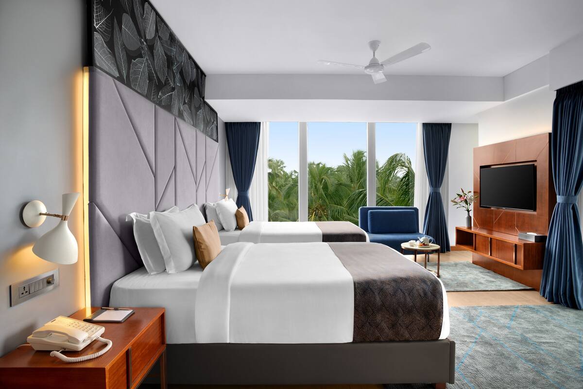 Una habitación de hotel con cama, lámpara de noche, teléfono y televisor sobre un mueble de madera.