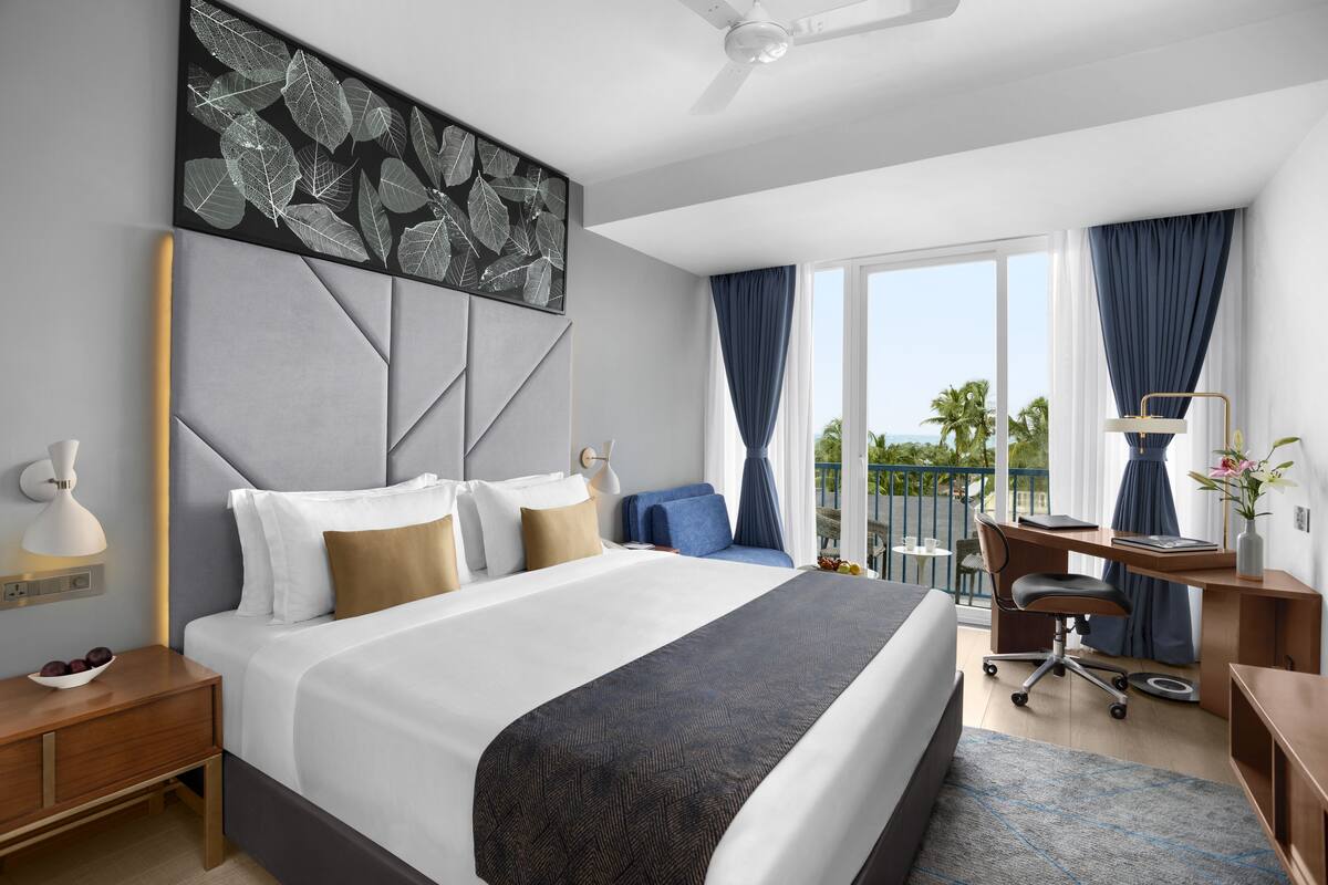 Una habitación de hotel moderna con una cama grande, un escritorio y un balcón con vistas.