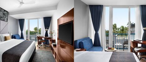 A hotel room with a bed, a desk, a TV, and a balcony with a view of palm trees.