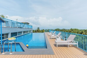 Zona de piscina con vistas a palmeras, sillas de descanso y una barandilla azul.