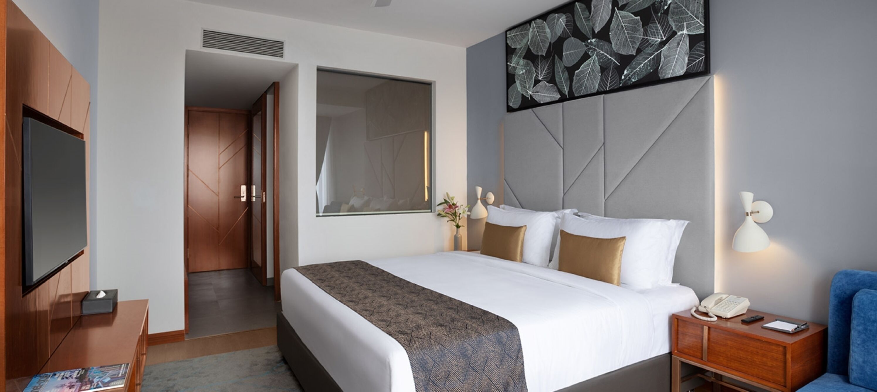 A modern hotel room with a large bed, a TV, a desk, and a window.