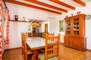 Un comedor con una mesa y sillas de madera, un armario con puertas de vidrio y una cocina al fondo.