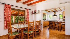 Un comedor con una mesa de vidrio y sillas de madera, una cocina con barra y vistas a zonas verdes.