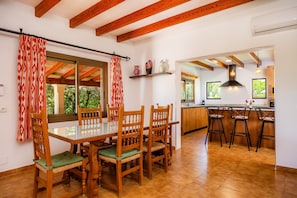 Un comedor con una mesa de vidrio y sillas de madera, una cocina con barra y vistas a zonas verdes.