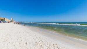 En strand med klar himmel, sandstrand och vågor som slår in mot land.