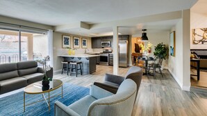 A modern living room with a sofa, armchairs, and a coffee table. A kitchen with a dining area is visible in the background. - Executive 5BR Retreat w 3 Ensuite, Pool & Spa, Air and Water Purifier, (Henderson)