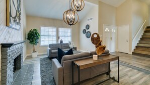 A spacious living room with a fireplace, a gray sofa, a coffee table, and a staircase leading to another level. - Executive 5BR Retreat w 3 Ensuite, Pool & Spa, Air and Water Purifier, (Henderson)