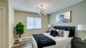 A bedroom with a bed, bedside tables, a potted plant, a window with blinds, a ceiling light fixture, and a framed picture on the wall. - Executive 5BR Retreat w 3 Ensuite, Pool & Spa, Air and Water Purifier, (Henderson)