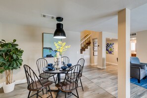 Un coin repas avec une table ronde, quatre chaises, un luminaire suspendu noir et une plante en pot.
