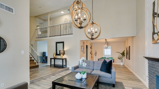 A spacious living room with a grey sofa, a coffee table, and a chandelier. There is a staircase leading to an upper level. - Executive 5BR Retreat w 3 Ensuite, Pool & Spa, Air and Water Purifier, (Henderson)