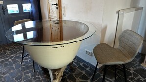 A round glass table with a cream-colored base, a chair with a cushioned seat, and a door with windows in the background. - Old miller's house by the windmill (Wittingen)