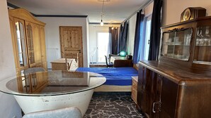 A compact room with a glass-top table, a wooden cabinet, a bed with a blue cover, and a stone-patterned floor. - Old miller's house by the windmill (Wittingen)
