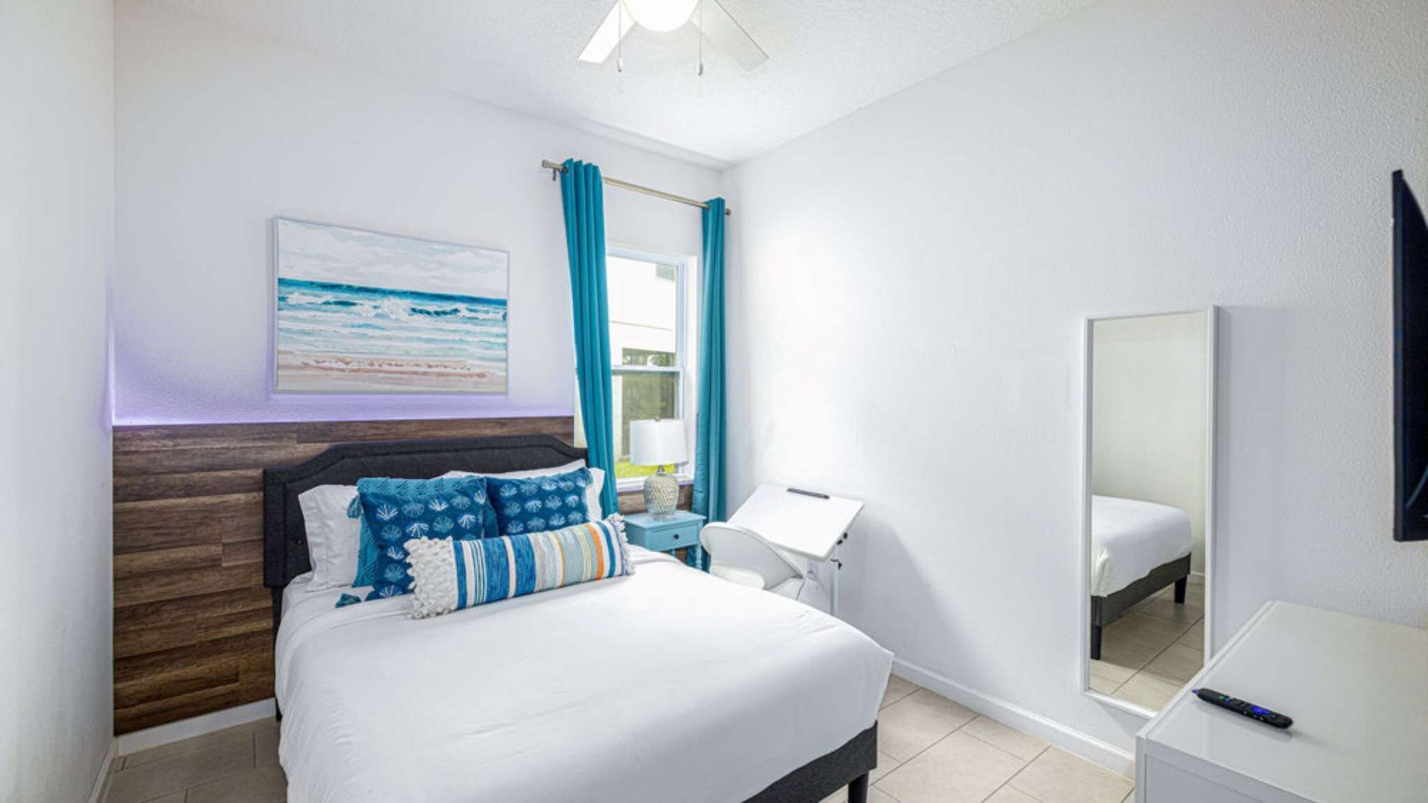 Ein Hotelzimmer mit Bett, Schreibtisch, Stuhl, Spiegel und einem Gemälde, das eine Strandlandschaft zeigt.