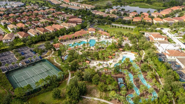 An aerial view of a residential area with a central swimming pool, tennis courts, and a winding water feature.