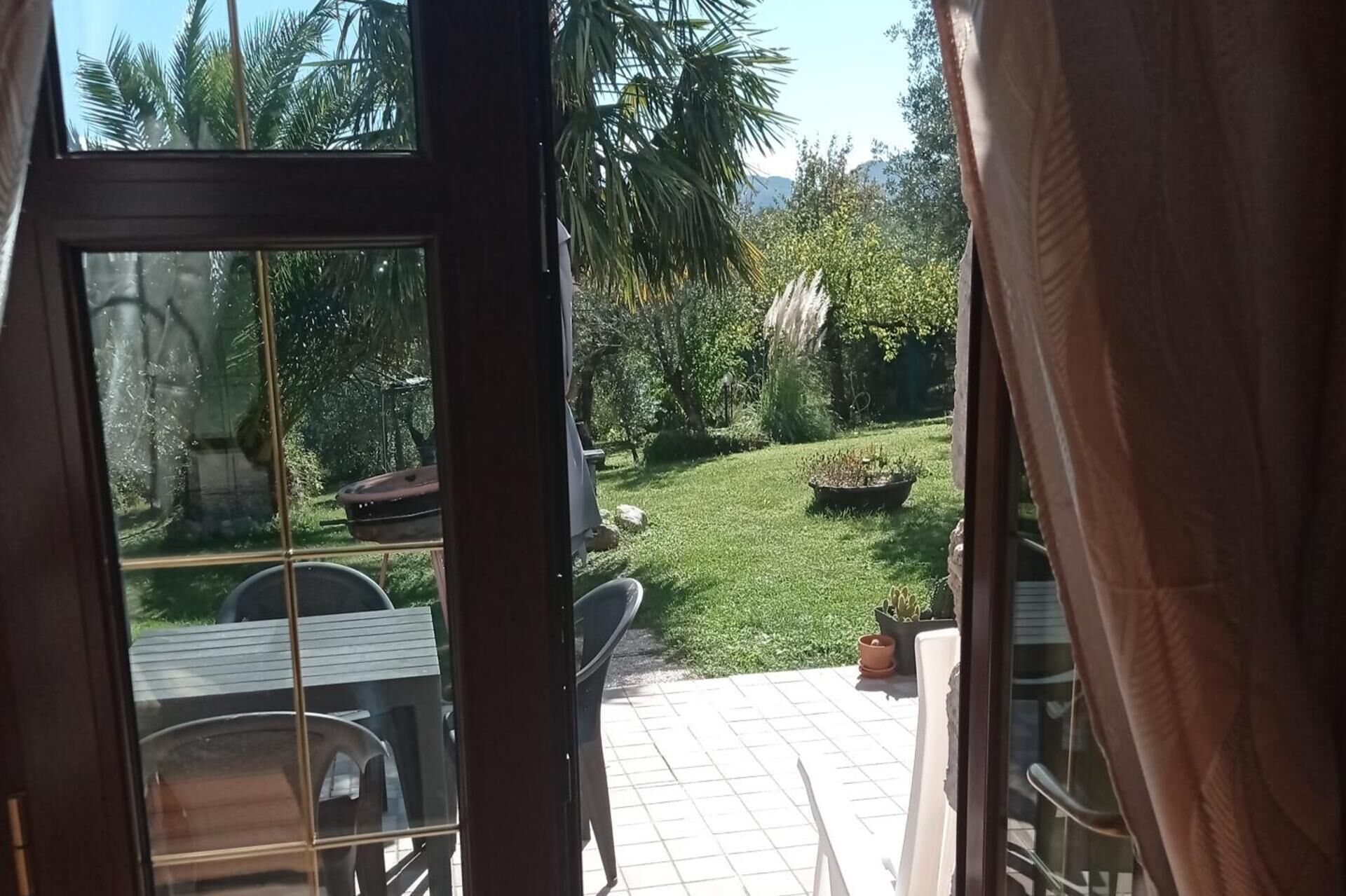 Eine Terrassenfläche mit Tisch und Stühlen, ein kleiner Garten mit Rasen und Blumentöpfen sowie ein Blick auf Palmen und Berge im Hintergrund.