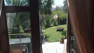 Eine Terrassenfläche mit Tisch und Stühlen, ein kleiner Garten mit Rasen und Blumentöpfen sowie ein Blick auf Palmen und Berge im Hintergrund.