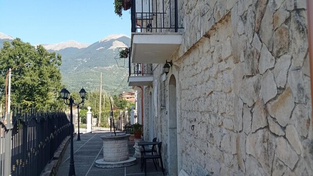 Une rue étroite bordée de bâtiments en pierre, avec une fontaine et une vue sur les montagnes.